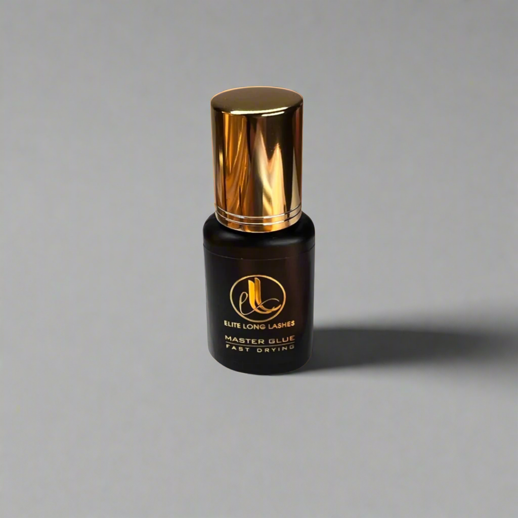 A bottle of Lash Blink Master Glue with a black label and a gold-colored cap, labeled for eyelash extensions in front of a gray background.