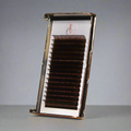 A tray of matte dark brown cashmere eyelashes arranged in rows, displayed in front of a gray background.