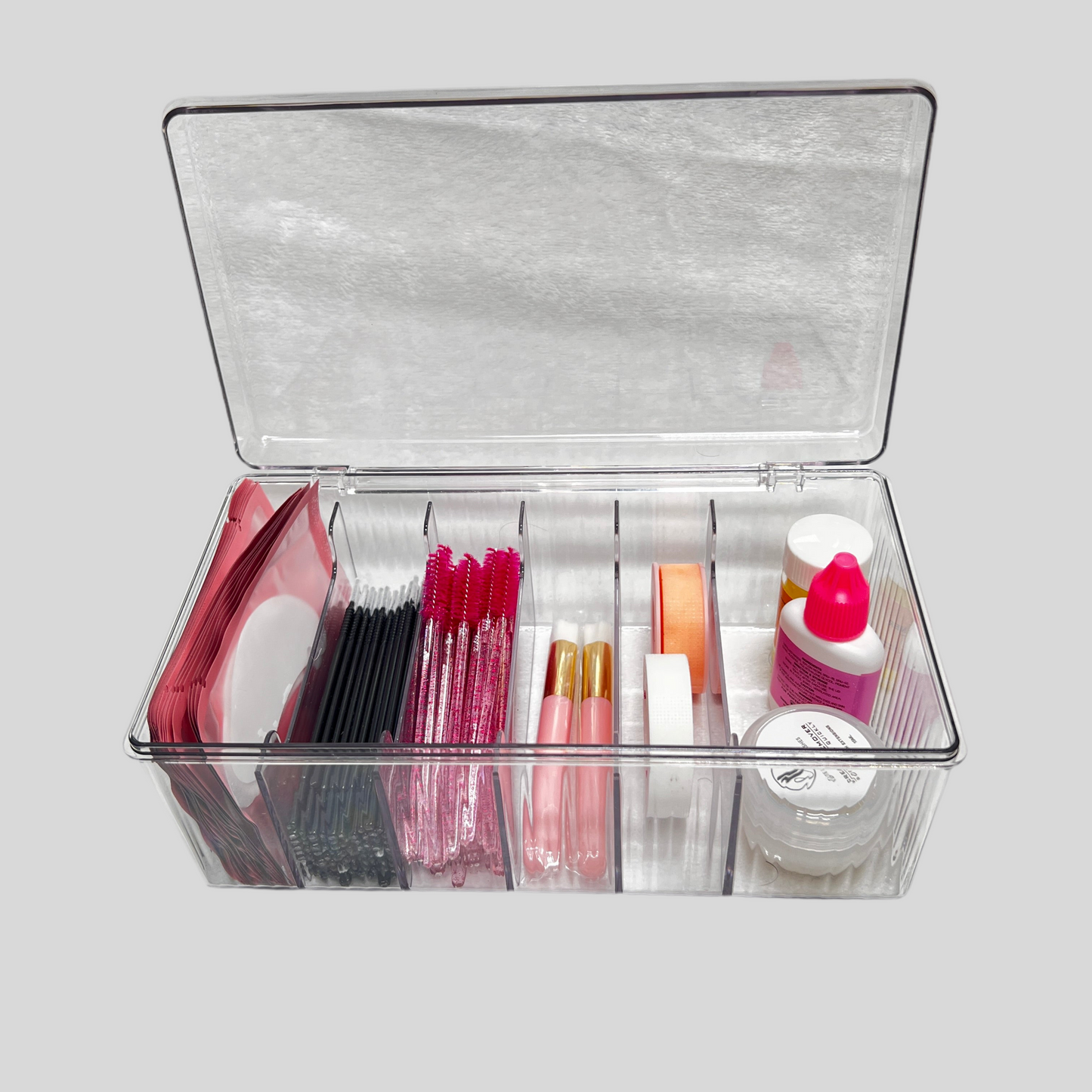 Clear plastic organizer with compartments containing lash products on a light gray background