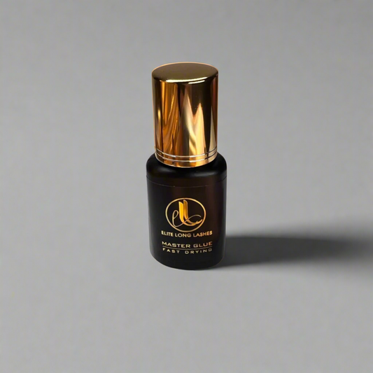 A bottle of Lash Blink Master Glue with a black label and a gold-colored cap, labeled for eyelash extensions in front of a gray background.