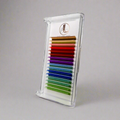 A tray of multicolored rainbow eyelash extensions arranged in rows, in a white tray with a gray background.