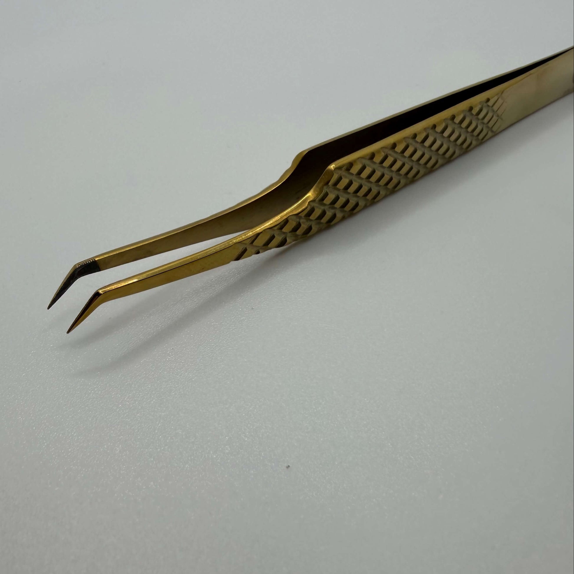 Gold-colored tweezers on a light gray background