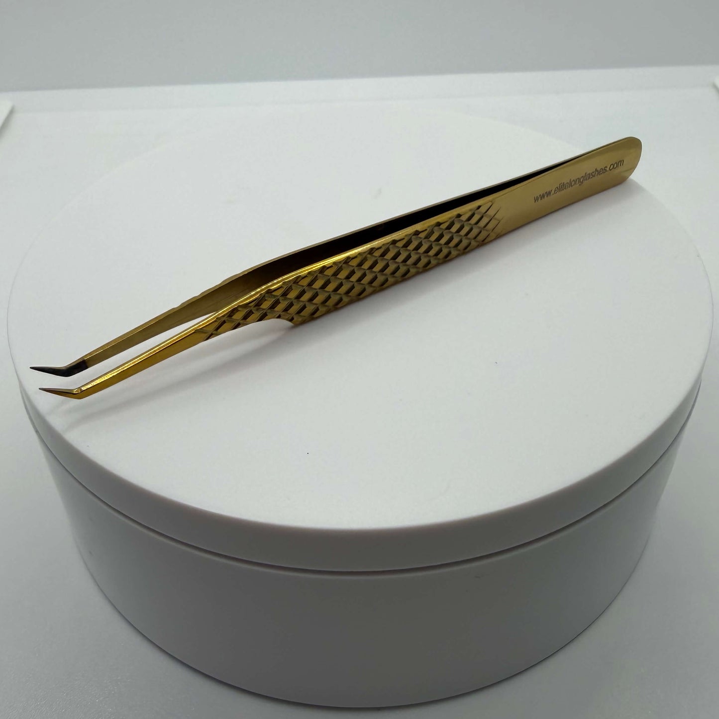 Gold tweezers on a white round container with a white background