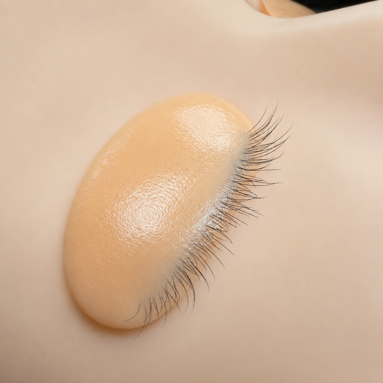 A close-up of a beige adhesive patch with black bristles along one edge, shown against a matching beige background.