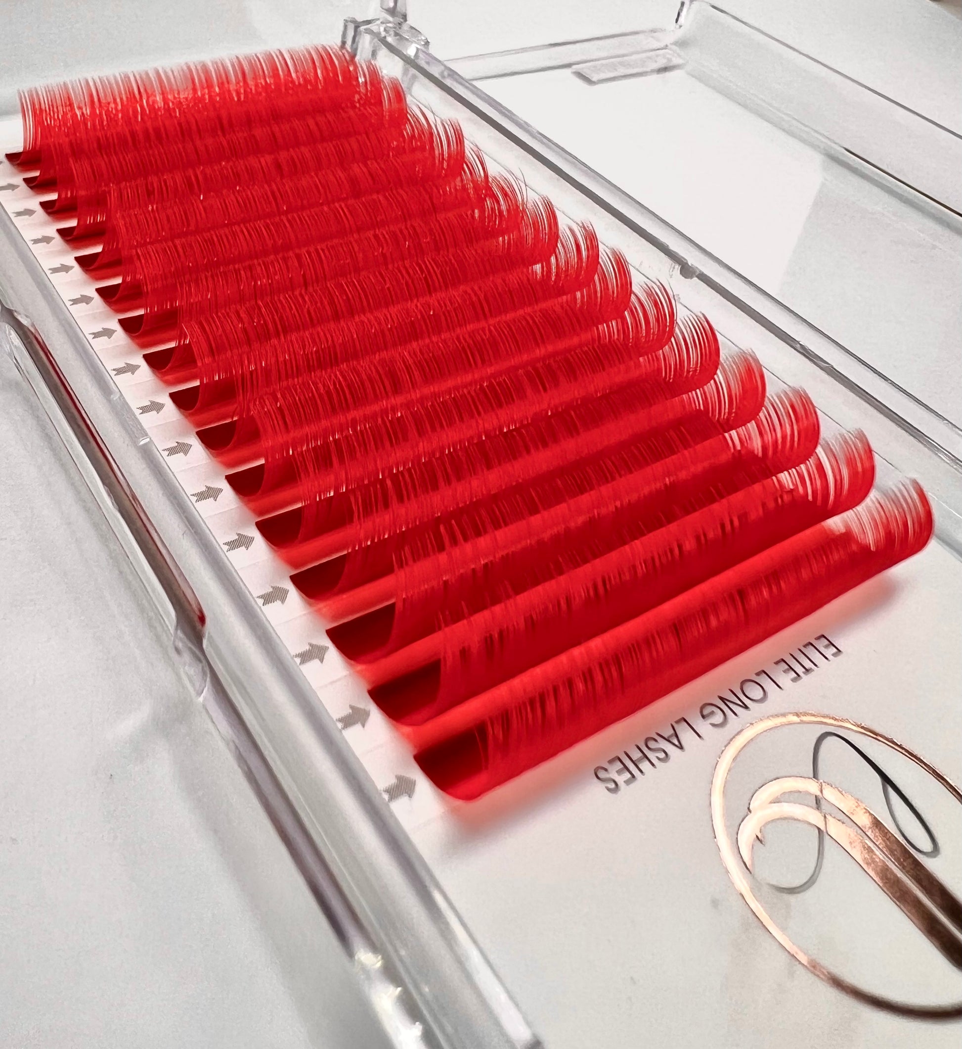 A tray of individual eyelash extensions, 16 rows. The eyelashes are candy red color. 