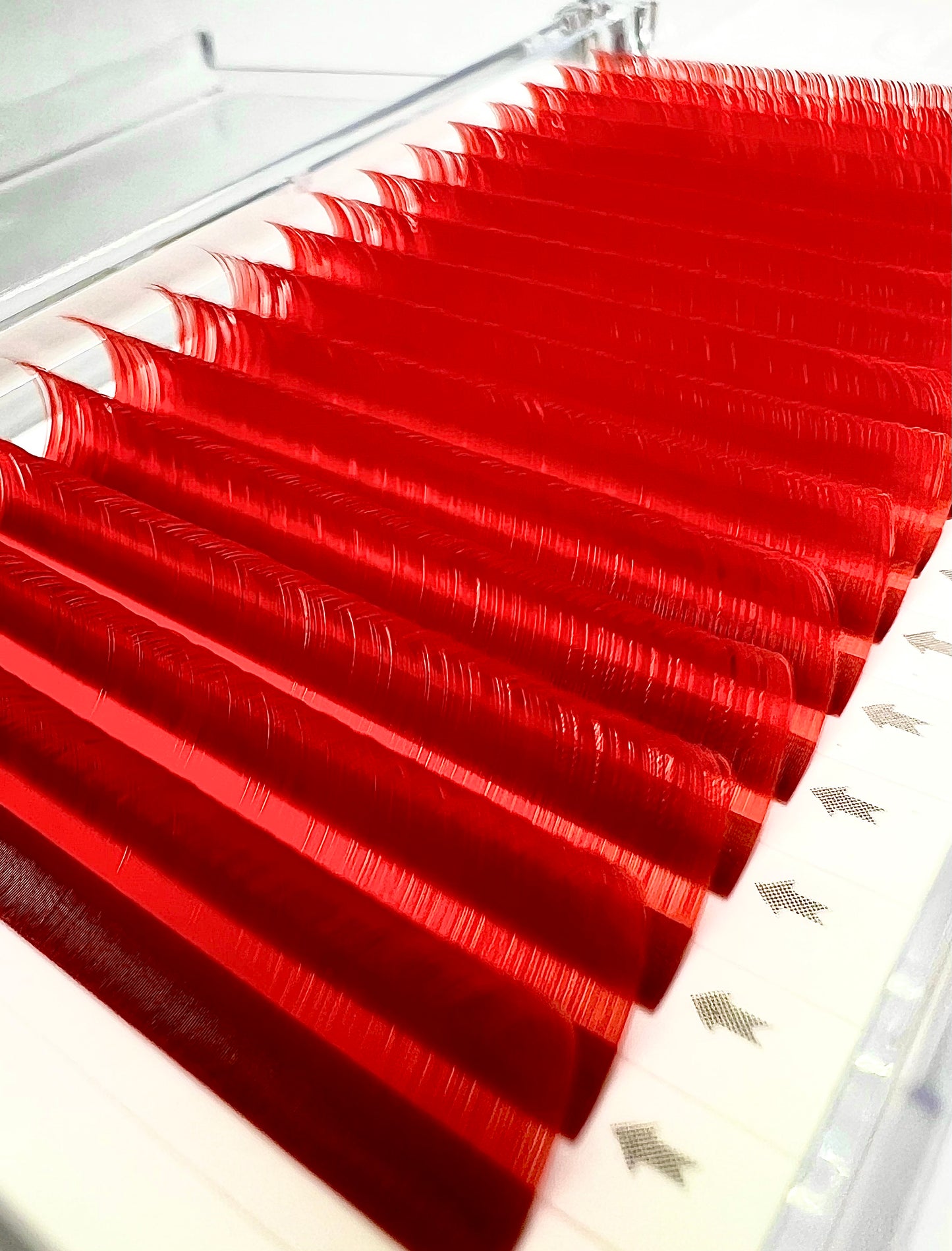 A tray of individual eyelash extensions, 16 rows. The eyelashes are candy red color. 